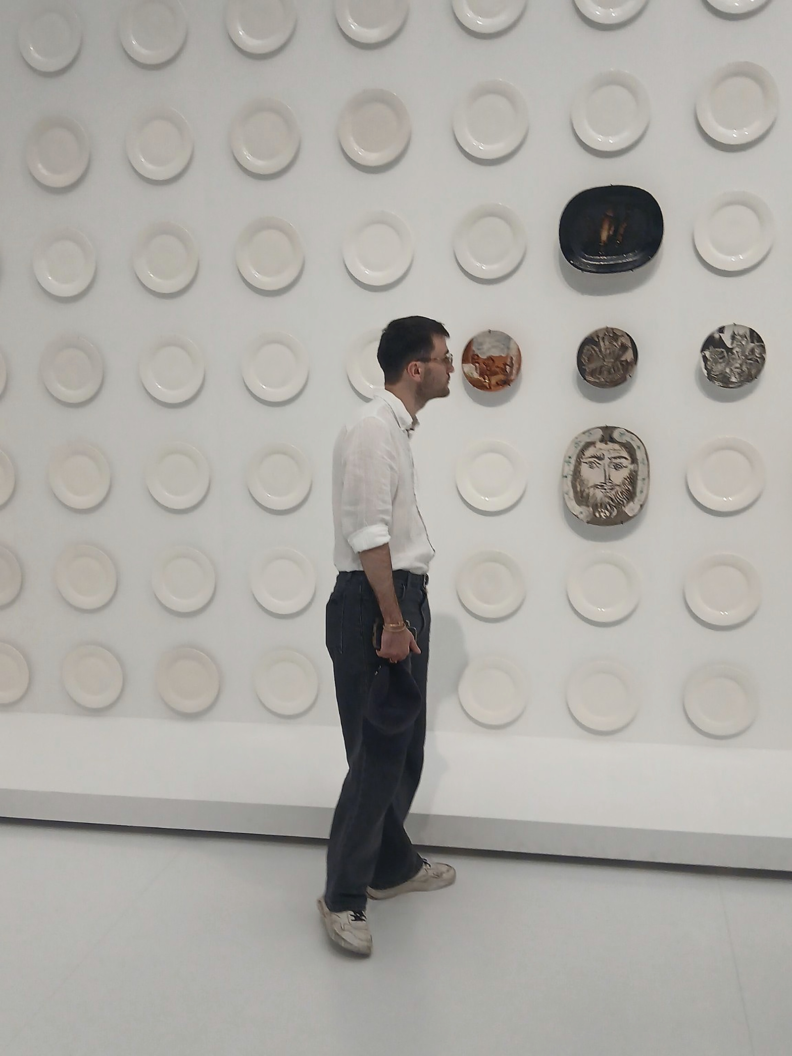 A visitor stops in front of a gallery wall covered with ceramic plates.