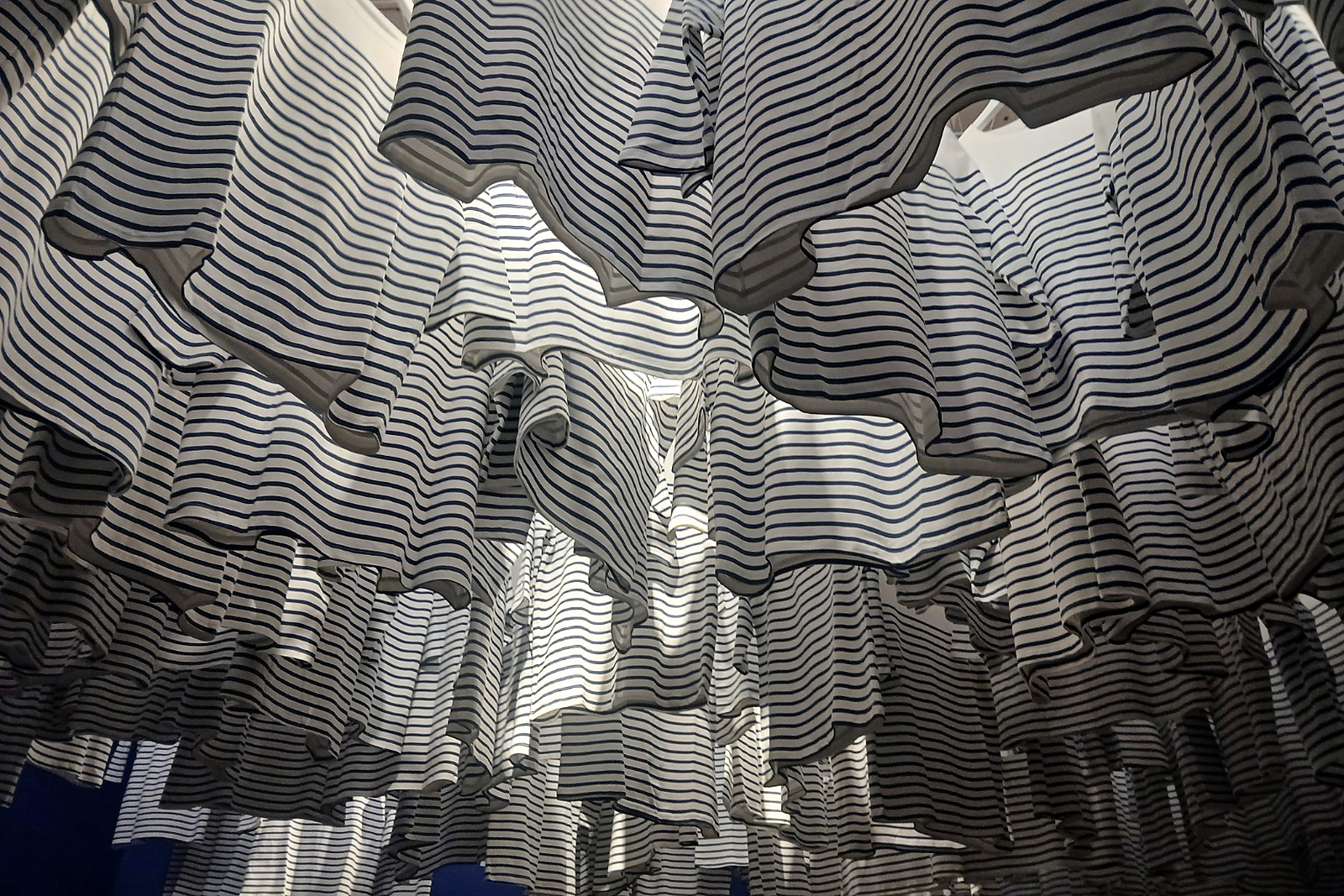 A striped textile installation hangs above the gallery in layered waves of light and shadow.